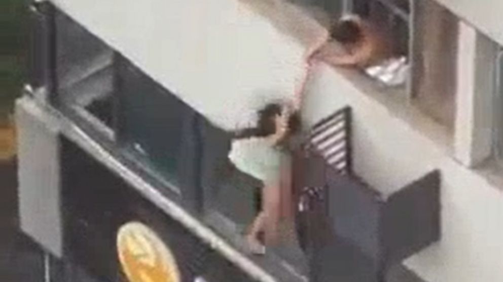 El video muestra la mujer balanceándose en el tercer piso del edificio, con un hombre intentando acercarla a la ventana.