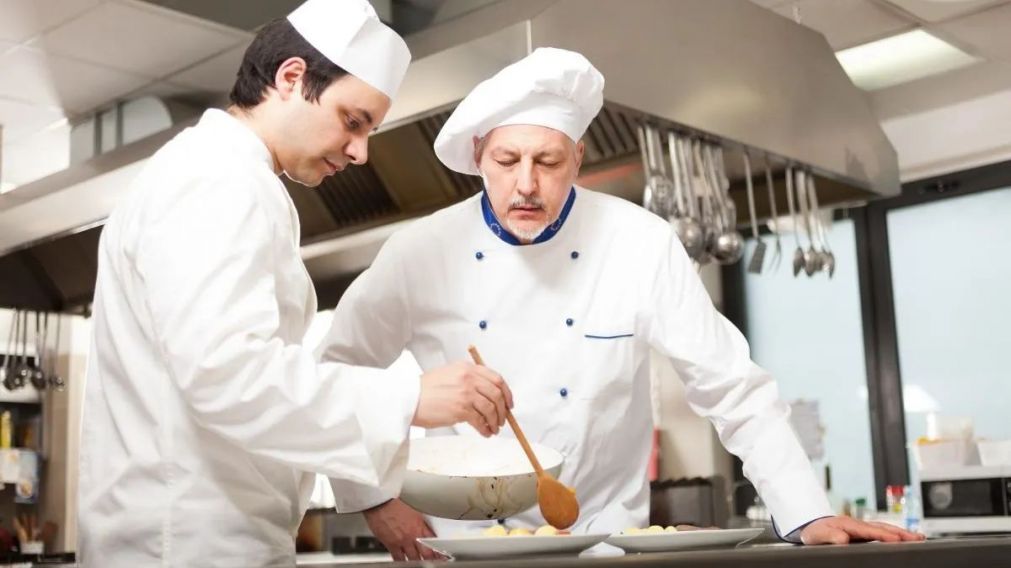 Chief chef watching his assistant garnishing a dish