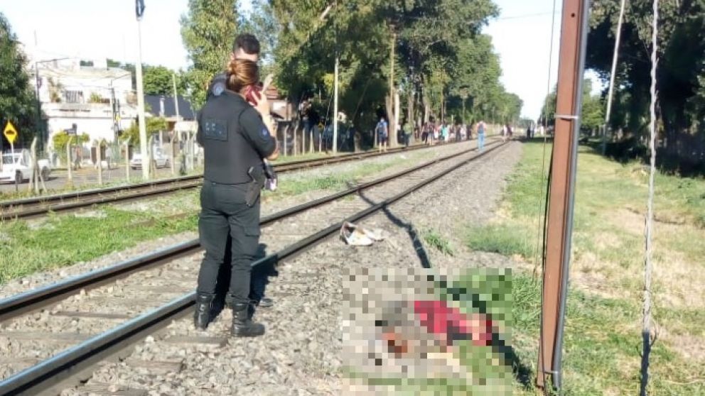 Los efectivos policiales observan al sospechoso del femicidio, que yace lesionado junto a las vías del tren.