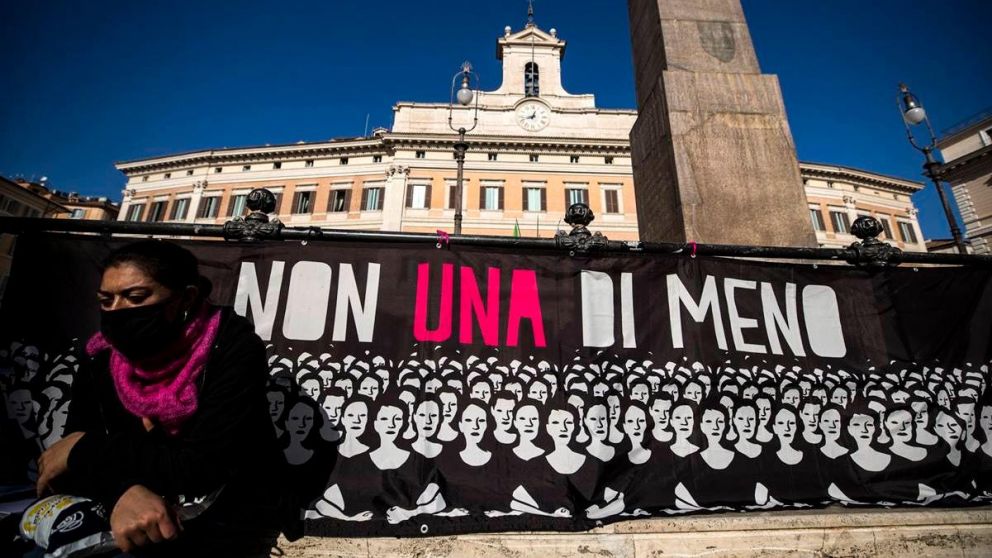 Una mujer sentada frente a una bandera gigante del Ni una menos, en Italia (Gentileza EFE).