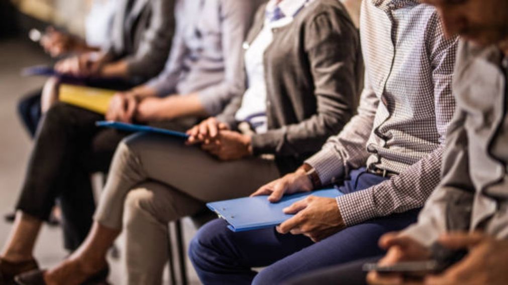 Large group of unrecognizable business people waiting for a job interview. Focus is on man with blue clipboard