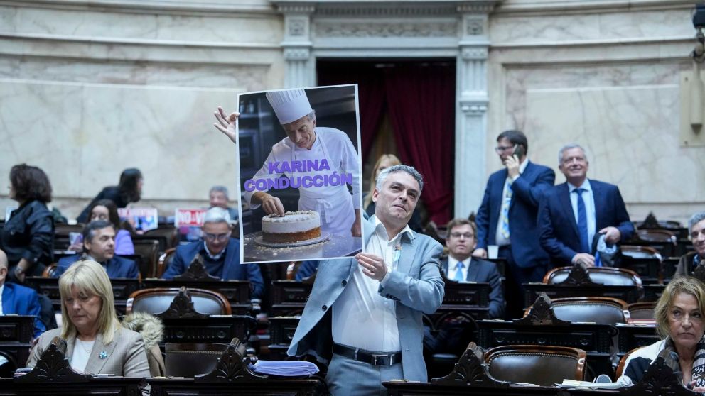 El diputado Esteban Paulón sostiene el cartel sobre Mauricio Macri y Karina Milei.