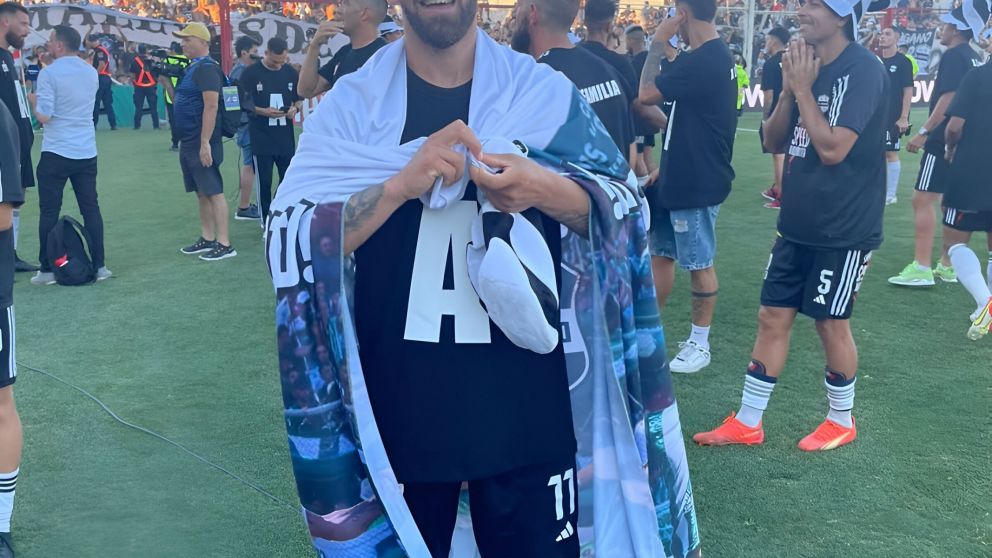 DOS PASIONES. EL DELANTERO POSA CON UNA BANDERA, EN LA CUAL SE DESTACAN ESCUDOS QUE LO IDENTIFICAN: RIESTRA Y LAFERRERE.